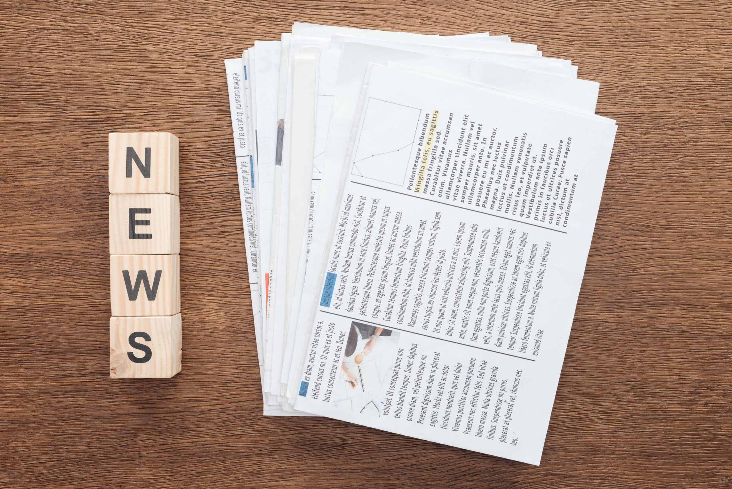 Newsletter : Bloc de lettres formant le mot "NEWS" à côté d'une pile de journaux, sur une table en bois.