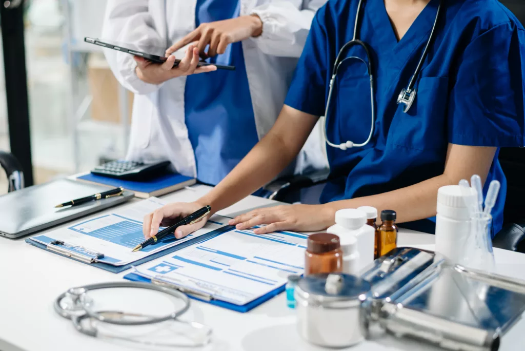 Professionnels de santé en tenue médicale analysant des documents et données cliniques lors d’une réunion ou d’une évaluation des pratiques professionnelles (EPP).