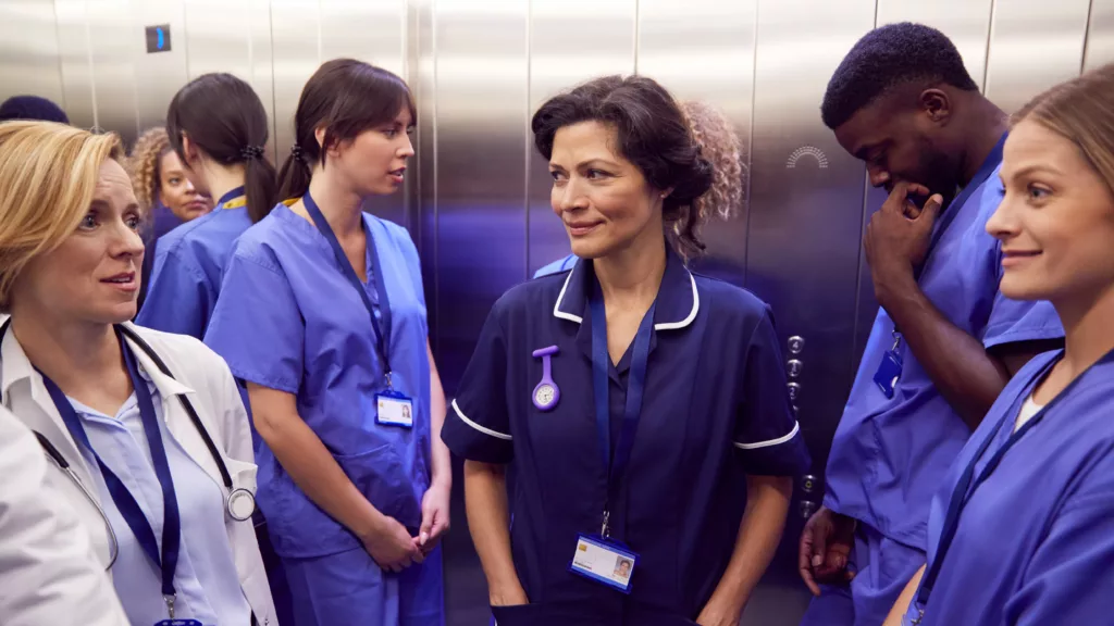 Réforme du diplôme Infirmier : Équipe d’infirmiers et professionnels de santé en tenue hospitalière échangeant dans l'ascenseur d'un établissement de soins, illustrant les enjeux de la réforme de la formation infirmière.