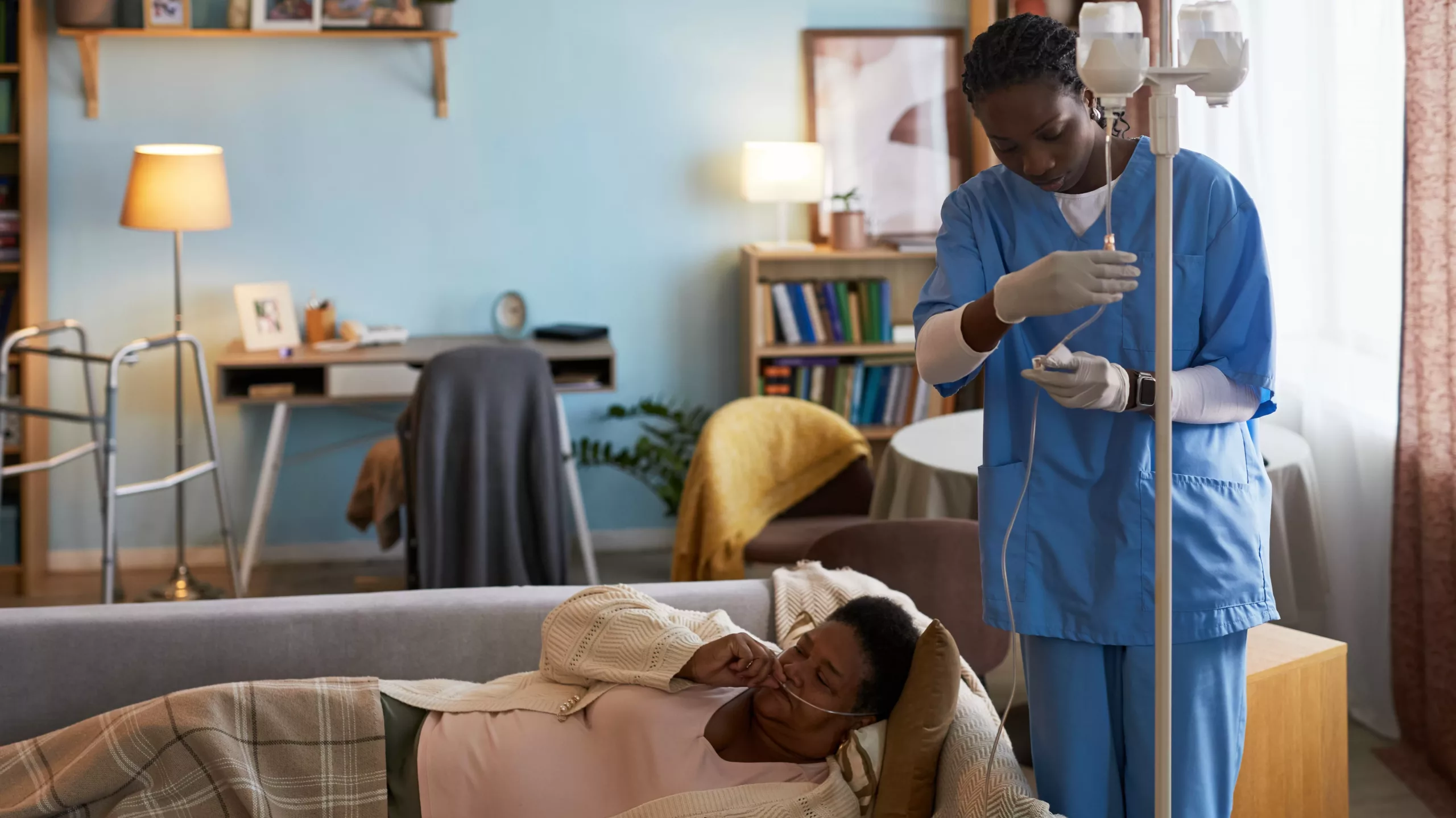 Infirmière à domicile réalisant une perfusion sur une patiente âgée allongée, illustrant la revalorisation des infirmiers dans les soins de proximité